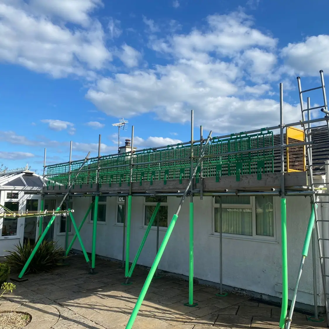 Residential roof scaffolding with green safety barriers installed on a bungalow