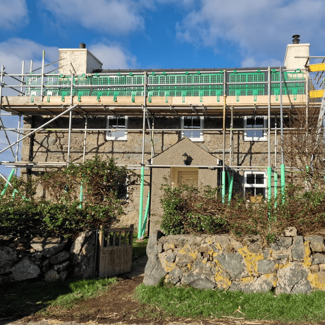 Green Scaffolding Group scaffold along the roof of a stone house