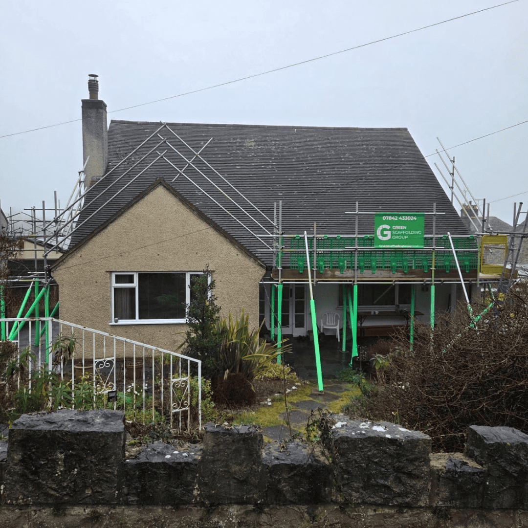 Scaffolding along the roof of a house, with green supports at the front
