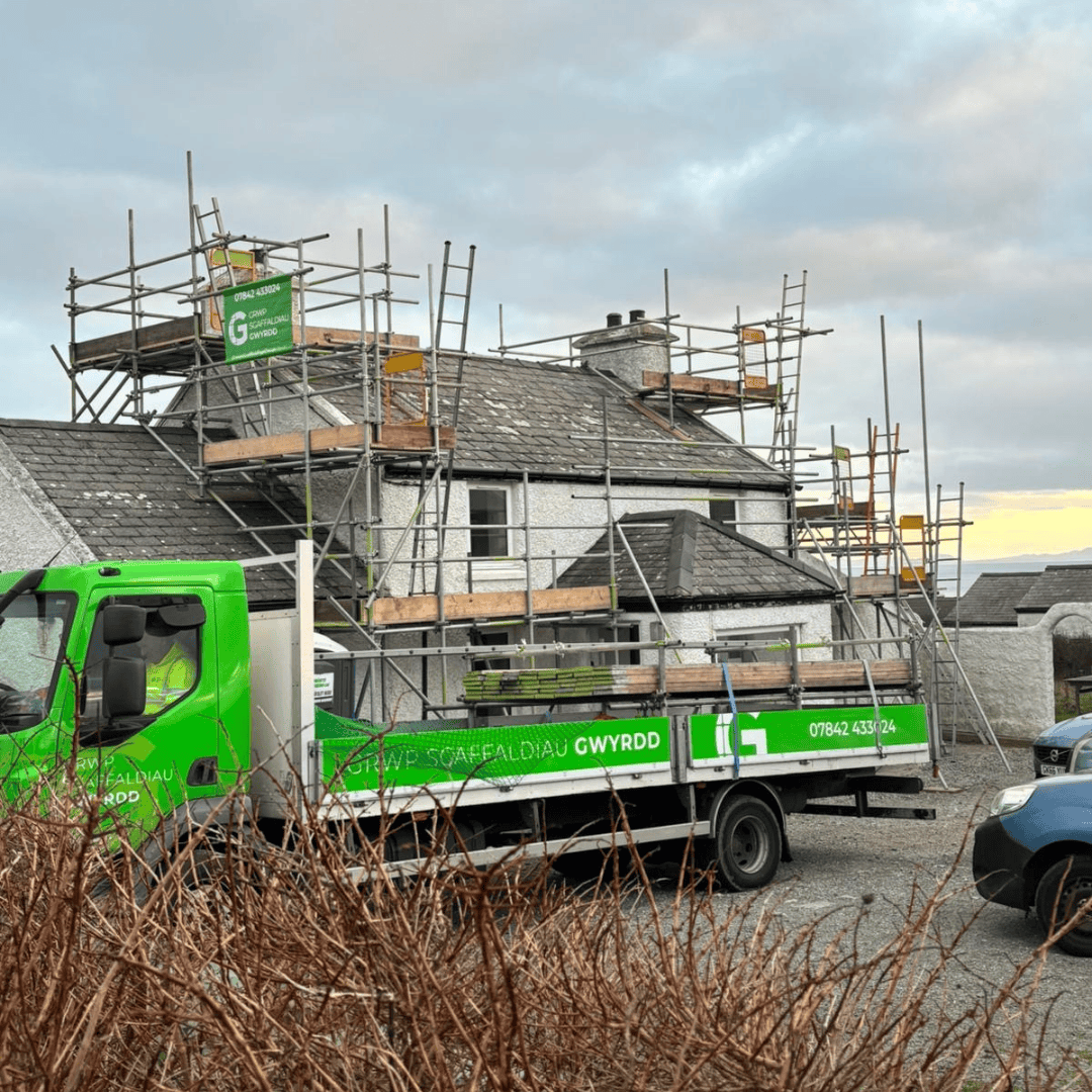Green Scaffolding Group lorry outside a house with scaffolding around its roof and chimneys