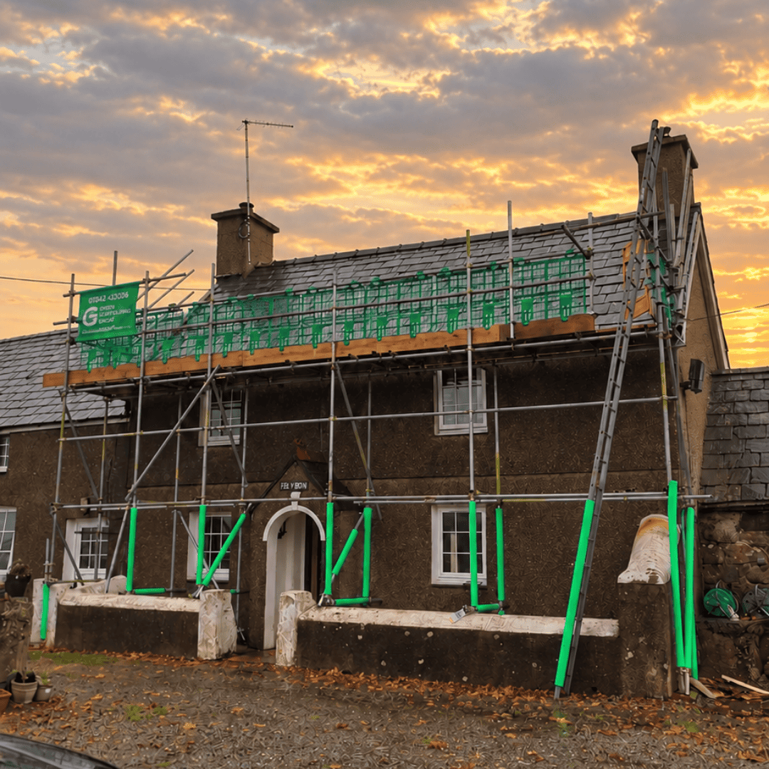 Green Scaffolding Group scaffolding along the roof of a house at sunset