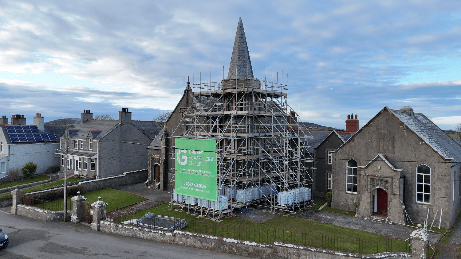 Scaffolding around a stone chapel tower beneath its pointed spire