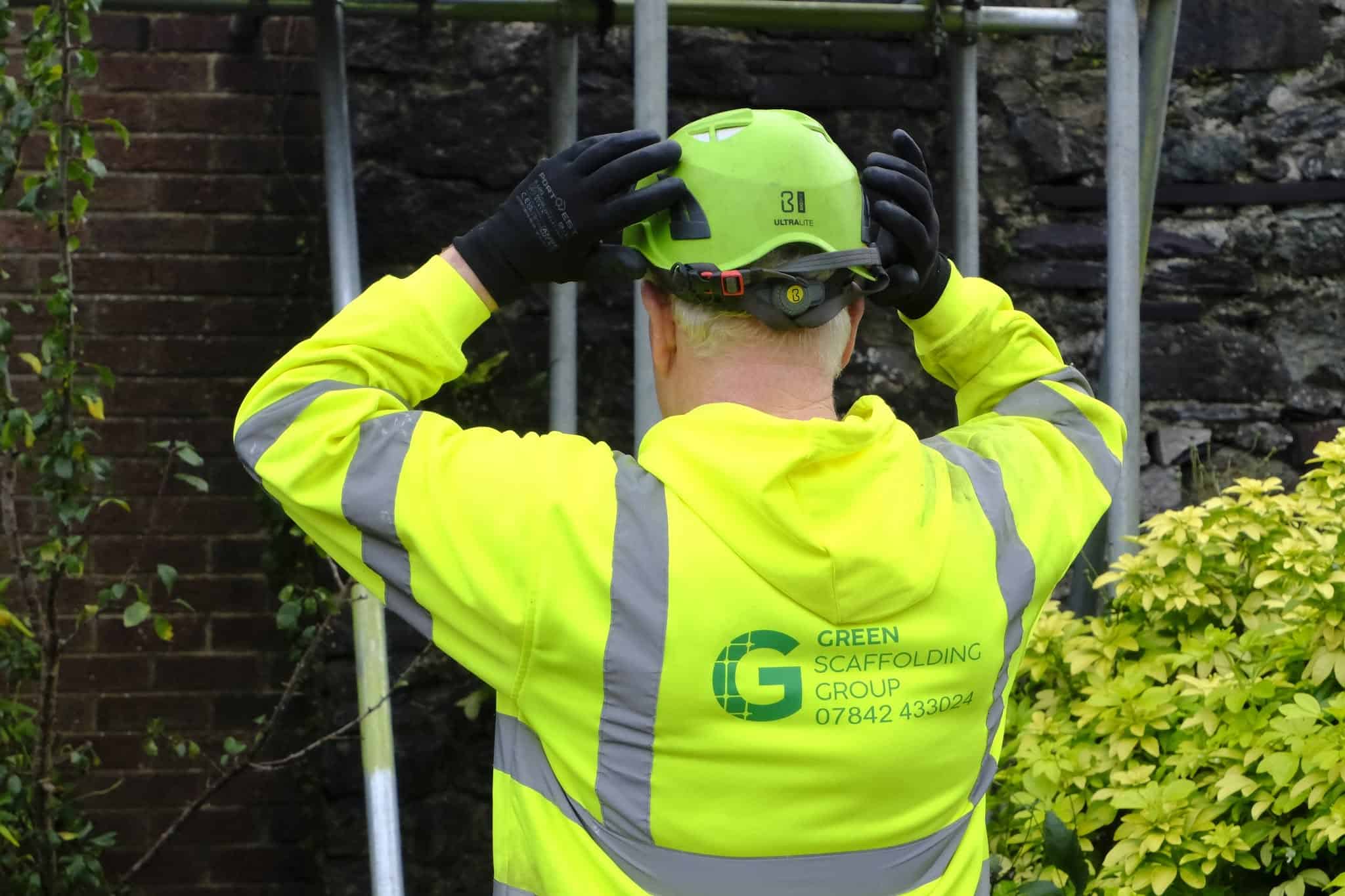 Green Scaffolding Group team member adjusting their safety helmet beside scaffolding
